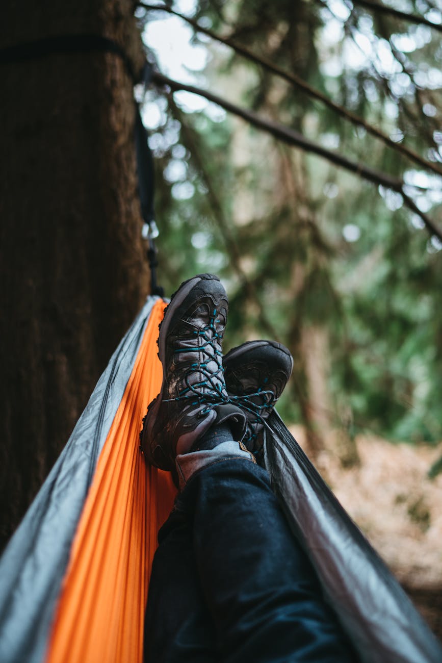 person wearing pair of black hiking shoes lying on orange and gray hammock